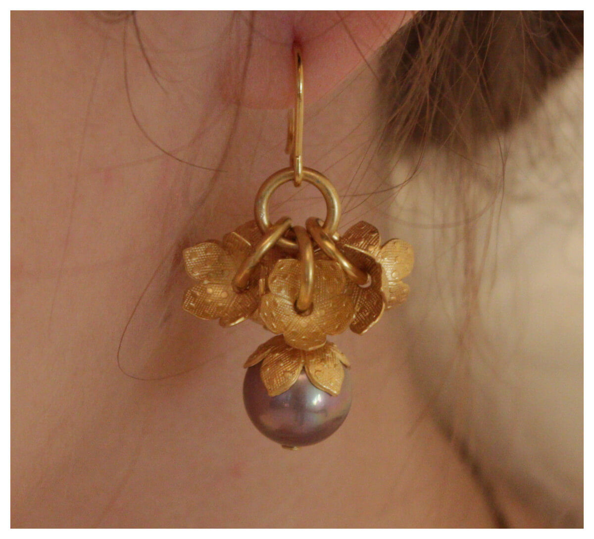 Preview: Ohrringe „Pompadour“ in Mauve mit 750er Goldauflage, getragen am Ohr – florale Elemente mit schimmernder mauvefarbener Perle.